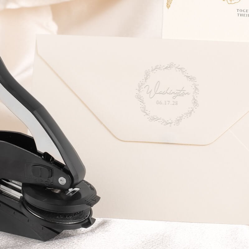 Embosser tool shown next to envelope that has been stamped with a custom wedding impression
