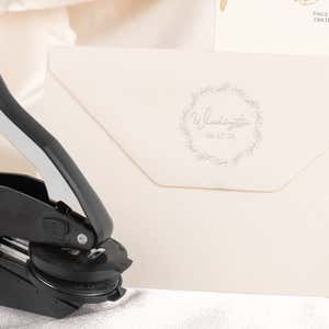 Embosser tool shown next to envelope that has been stamped with a custom wedding impression