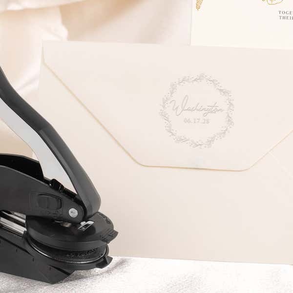 Embosser tool shown next to envelope that has been stamped with a custom wedding impression