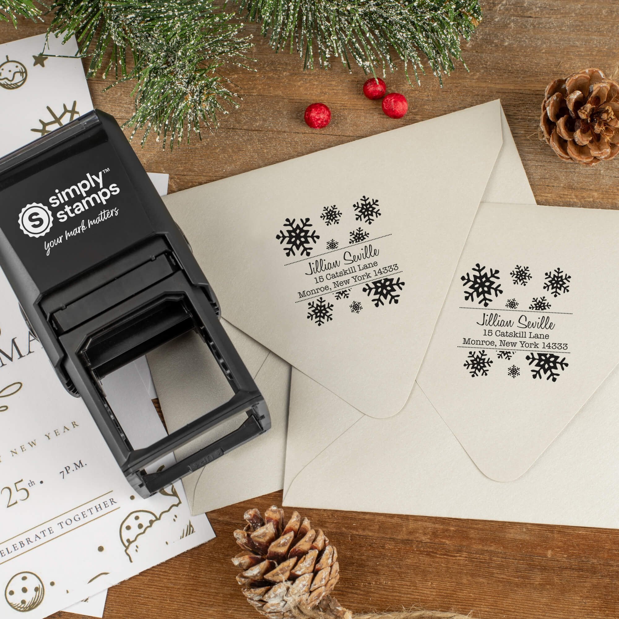 Holiday-themed ‘Seville Snowflakes’ address stamp shown on envelopes beside festive stationery, pinecones, and decorations.