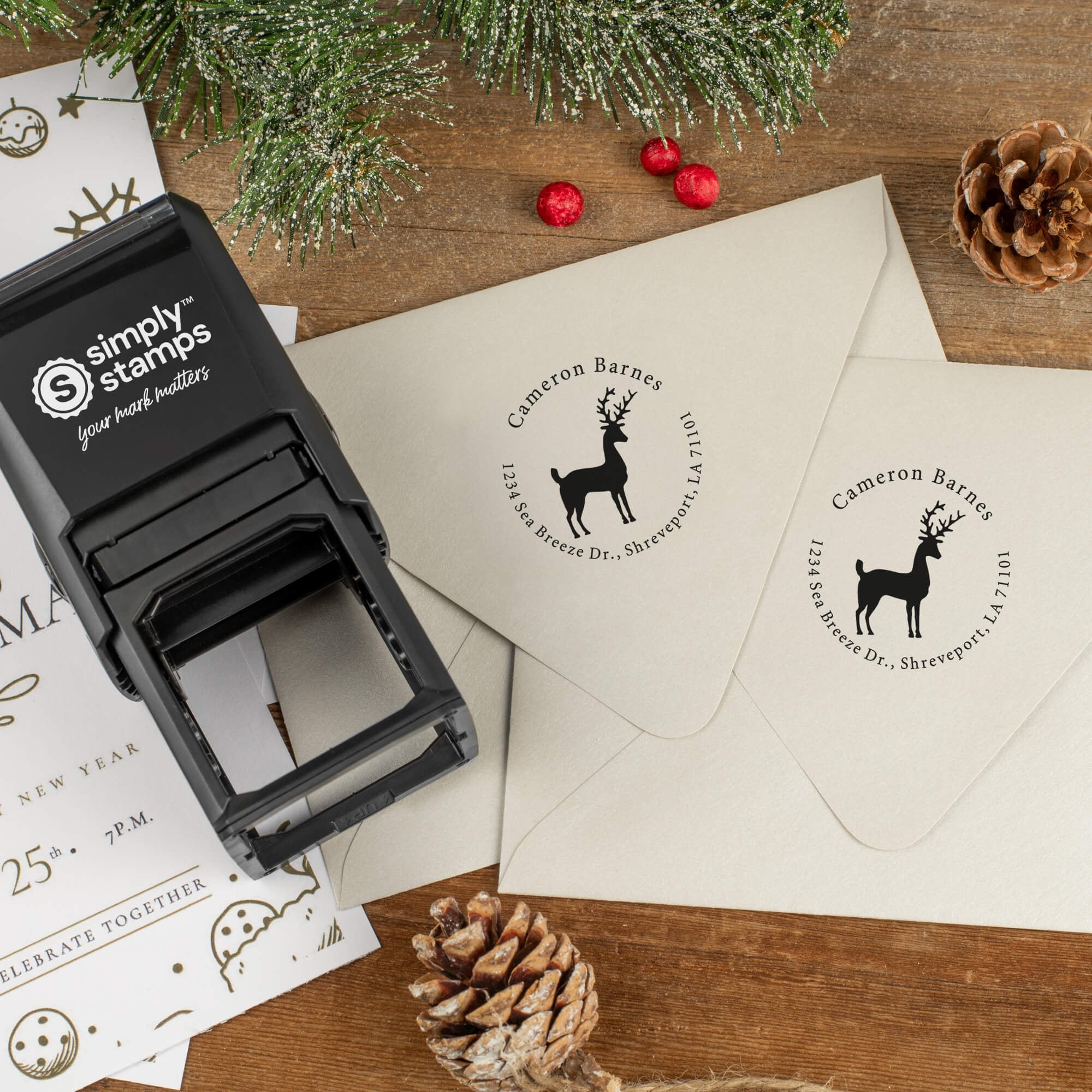 Holiday-themed ‘Stag Reindeer’ address stamp shown on envelopes beside festive stationery, pinecones, and decorations.