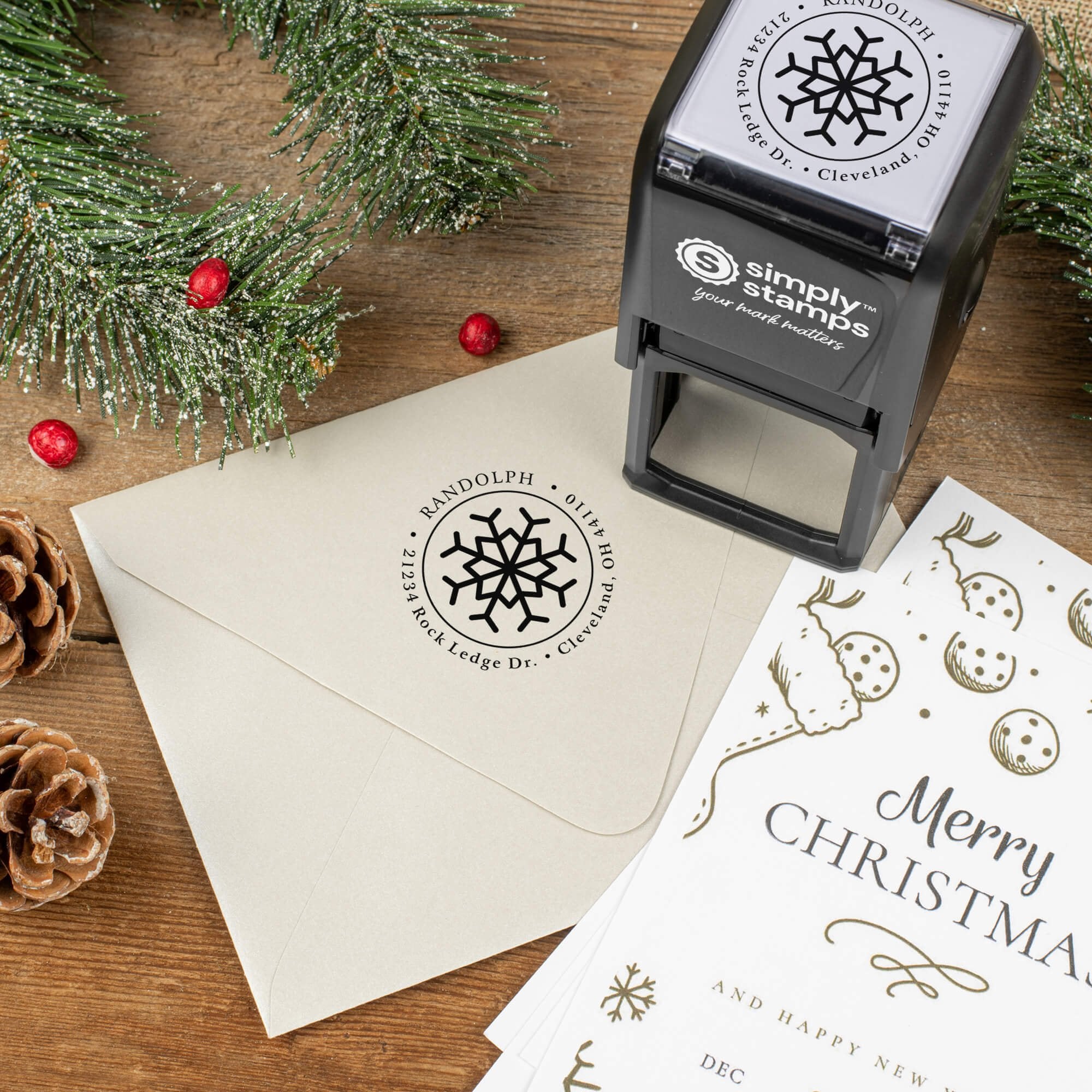 Holiday-themed ‘Eight Point Snowflake’ address stamp shown on envelopes beside festive stationery, pinecones, and decorations.