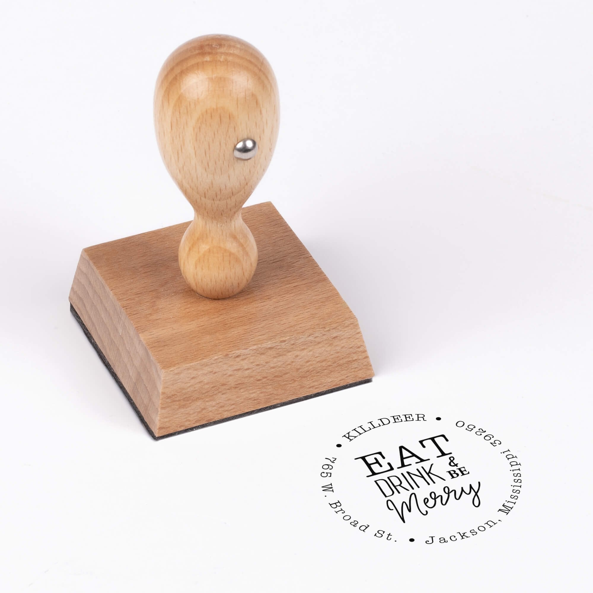 European wood hand stamp shown from above featuring custom ‘Eat Drink and Be Merry’ holiday return address design.