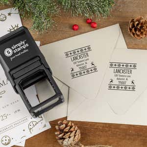 Holiday-themed ‘Designer Reindeer’ address stamp shown on envelopes beside festive stationery, pinecones, and decorations.