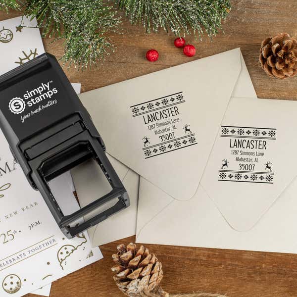 Holiday-themed ‘Designer Reindeer’ address stamp shown on envelopes beside festive stationery, pinecones, and decorations.