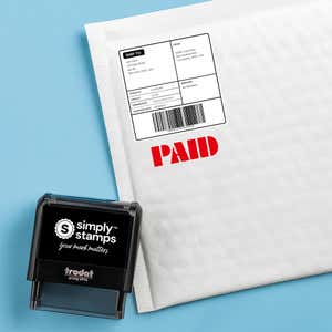 Red “PAID” stamped on a white padded mailer; self-inking office stamp shown beside the package