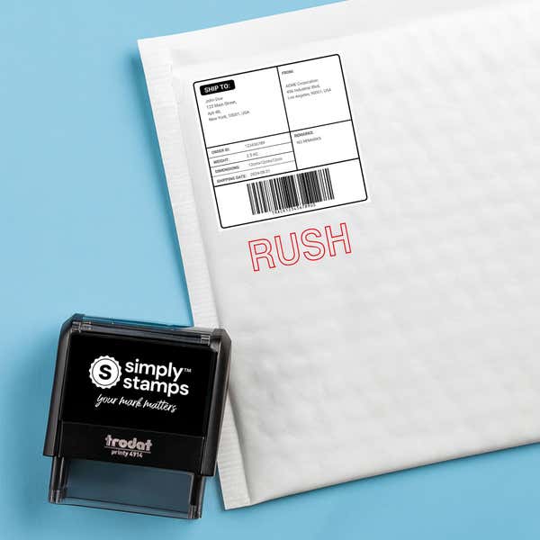 Red outline RUSH stamped on a white padded mailer with a self inking stamp beside it