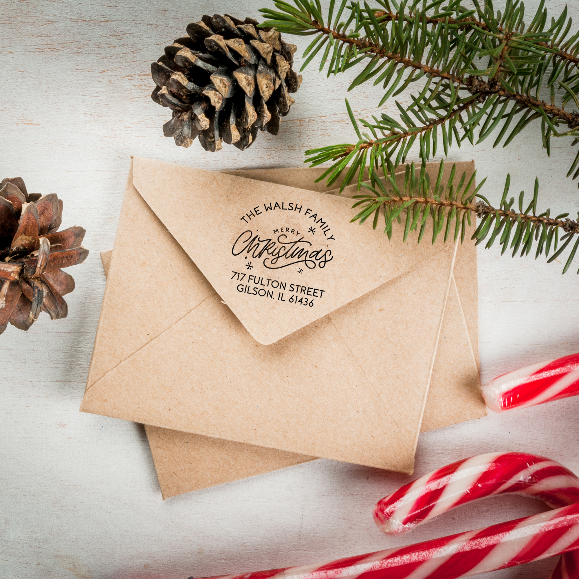 Christmas address stamp on a kraft envelope next to holiday greenery