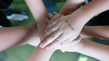 Children putting their hands together with a stamp that shows the name of their teacher on it